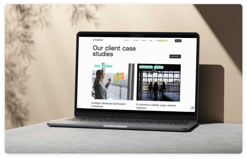 A laptop on a concrete surface displays a webpage titled ‘Our client case studies,’ showcasing two examples: ‘Intelligent Workload Optimization Framework’ and ‘E-commerce visibility surge: website migration.’ The background is softly blurred with natural tones and plant shadows.