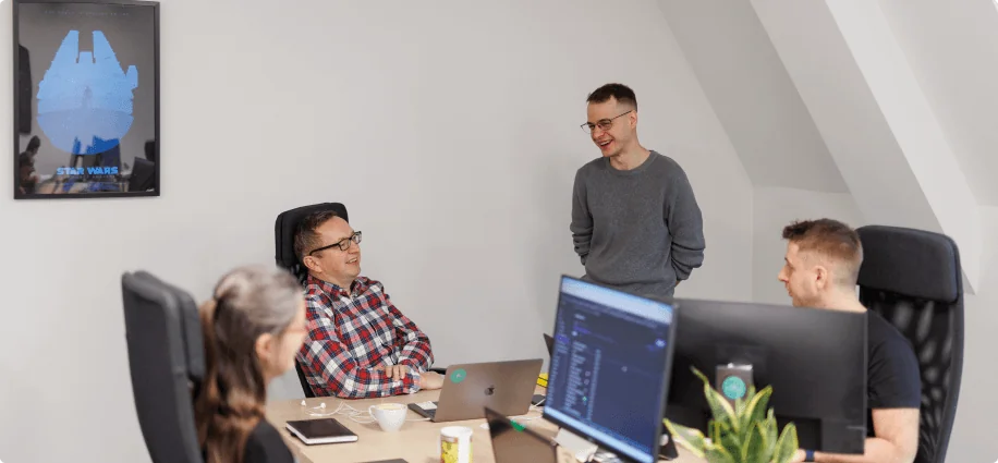 The image captures a casual office environment where four colleagues are engaged in a friendly conversation.